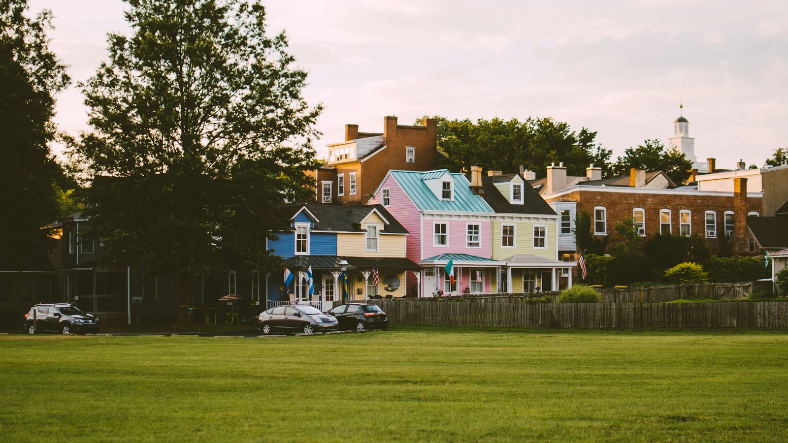 A row of pastel wood-frame houses with porches across a green in New Castle, Delaware