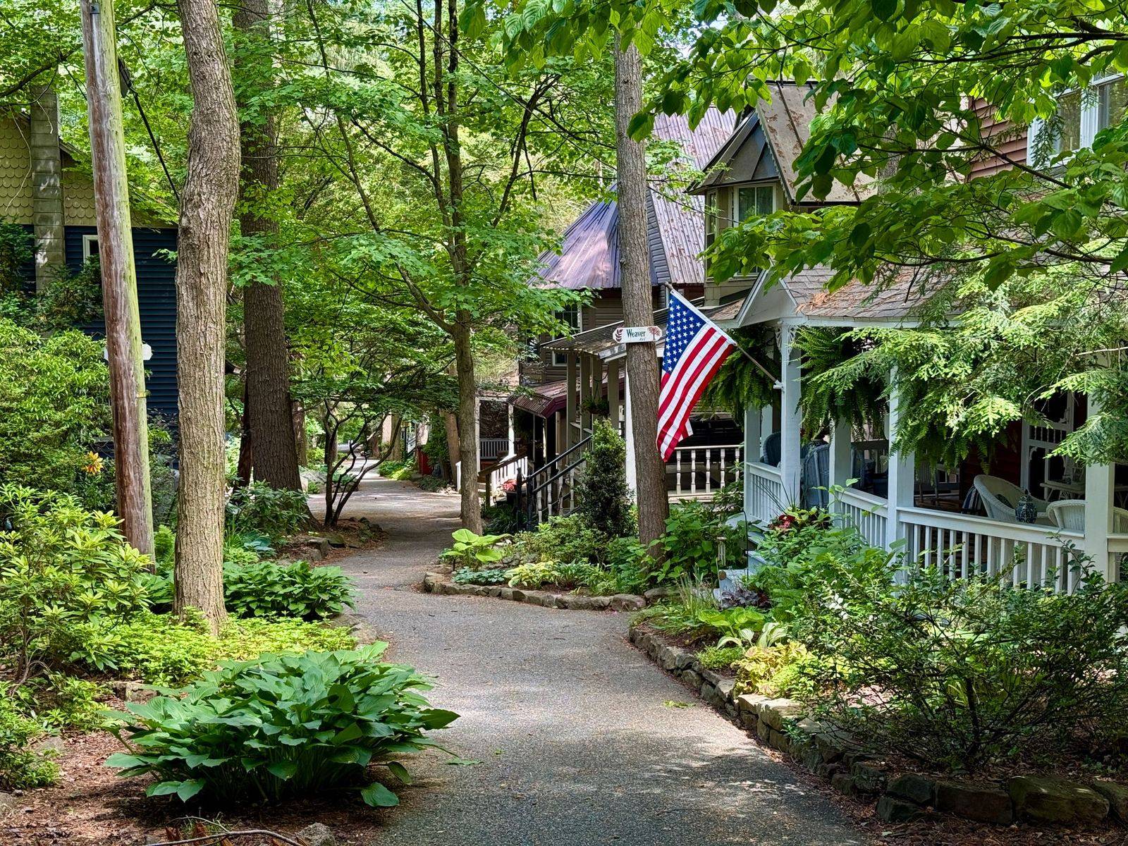 Tree-lined path past porch-front cottages with an American flag