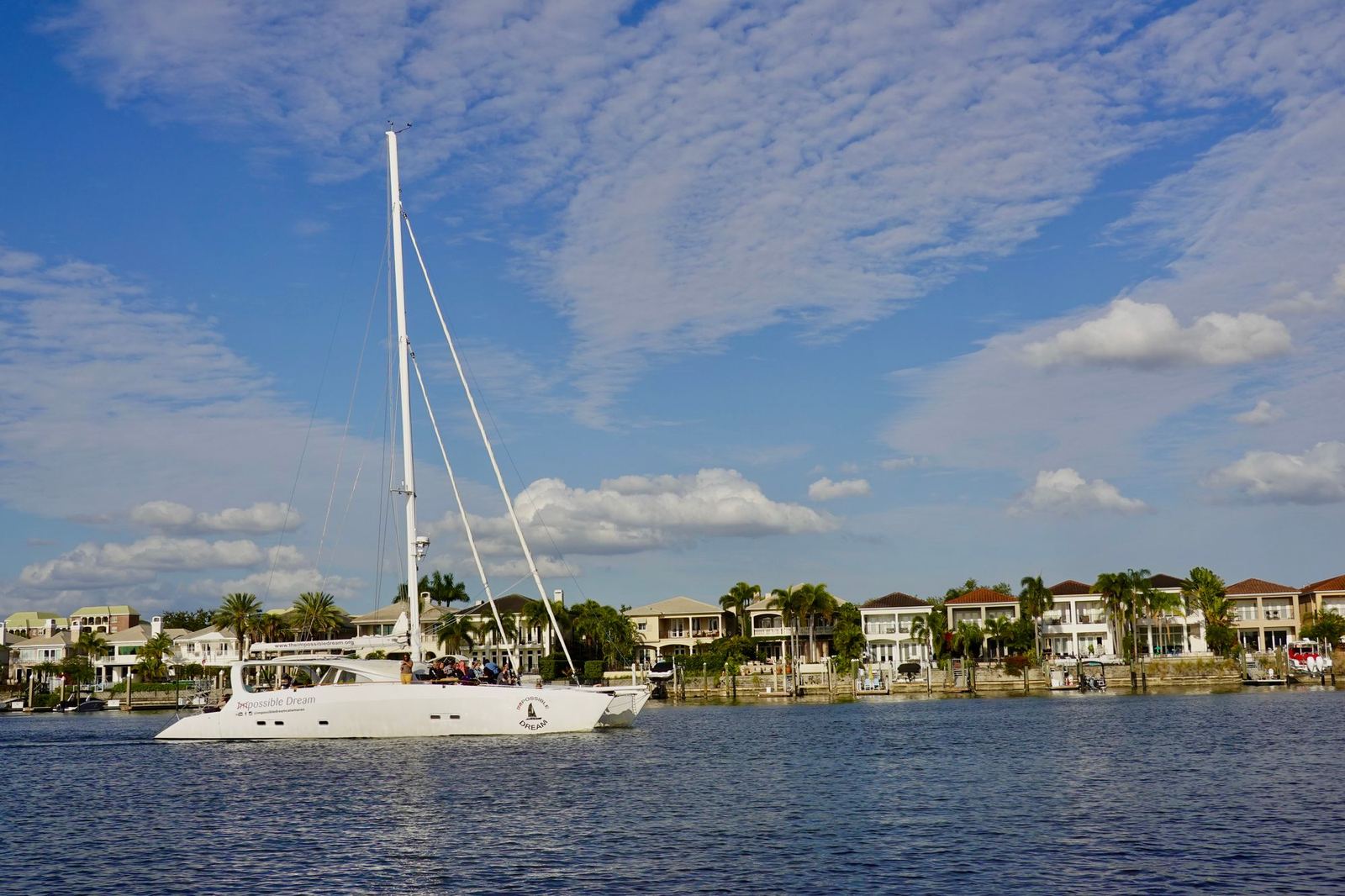 Waterfront homes with palms along Tampa Bay as a sailboat passes